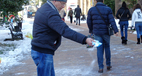 Прохожий посыает улицу солью, купленной в магазине. Фото Светланы Кравченко для "Кавказского узла"