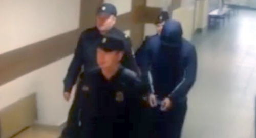 Полицейские ведут Магомеда Гучигова на заседание суда. Скриншот видеозаписи из южета телеканала НТВ, Ntv.ru/video