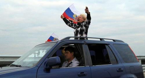 Женщина держит российский флаг , проезжая по мосту в Крым. Фото REUTERS/Pavel Rebrov