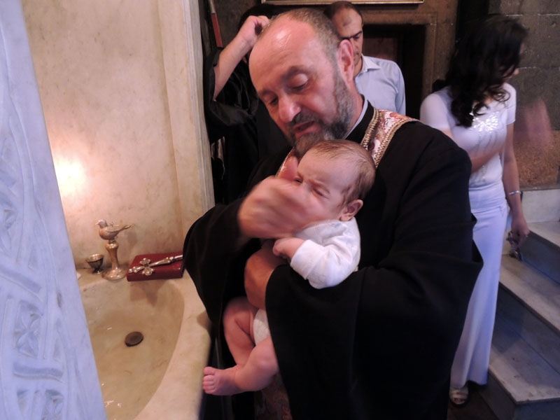 Священник протирает водой лоб малыша.
