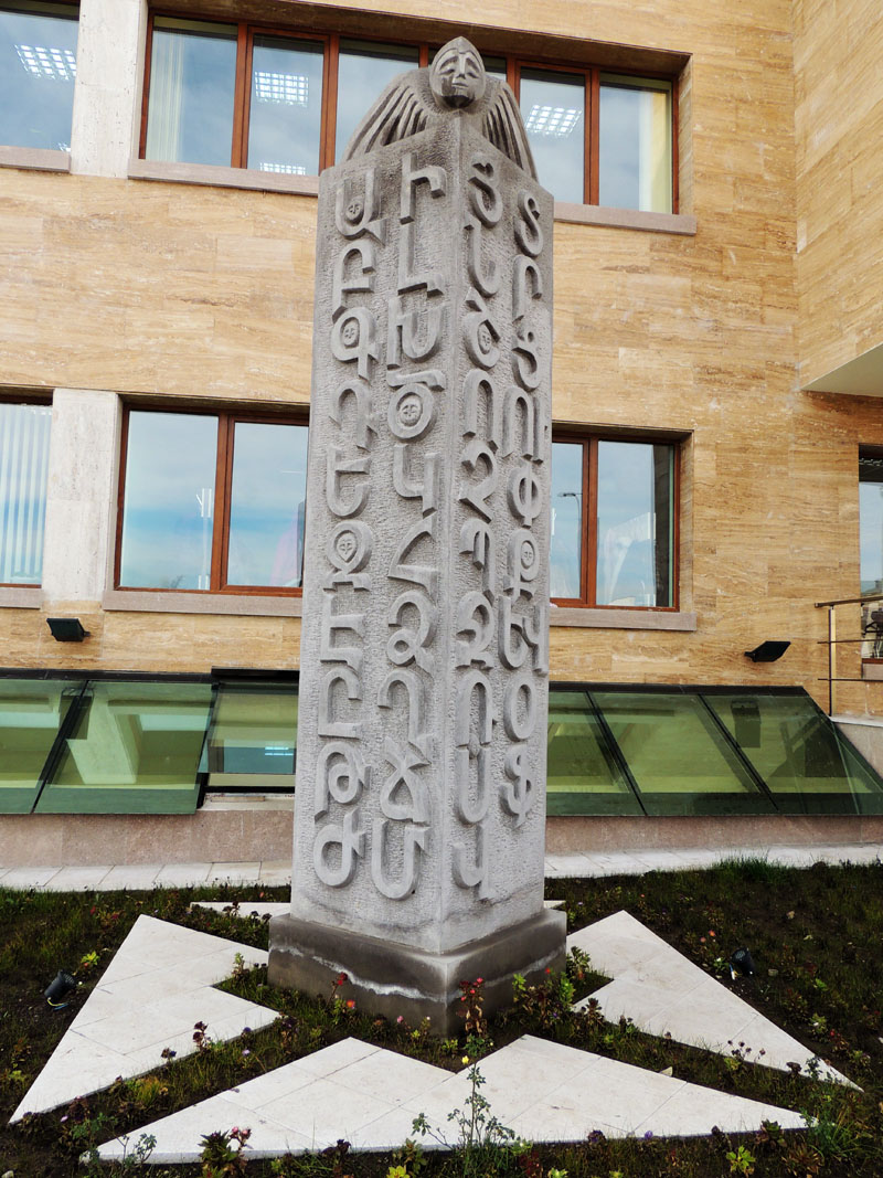 Памятник вл дворе школы, на котором изображены буквы армянского алфавита.