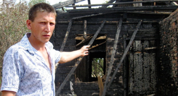 Виталий Богданов показывает наполовину сгоревший барак и кирпичную стену справа, которая спасла их квартиру от огня. Астрахань, Приволжский район, поселок Стеклозавода, 19 июня 2012 г. Фото Вячеслава Ященко для "Кавказского узла"
 