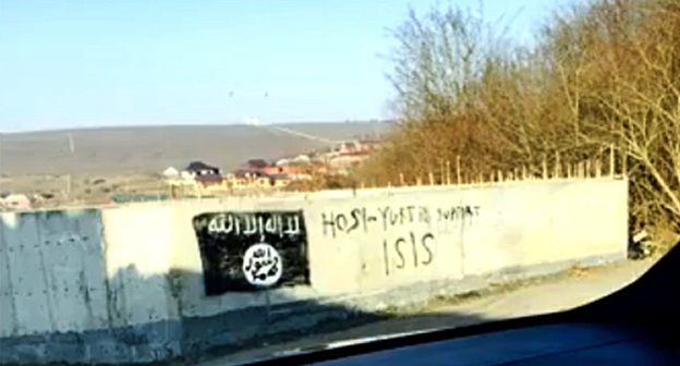 Изображение флага, используемого боевиками «Исламского государства» (признанного 29 декабря 2014 г. Верховным судом России террористической организацией), на стене в селении Хосе-Юрте. Фото: Стоп-кадр видео ИГИШ в Хоси -Юрте / IG in Chechnya, http://www.youtube.com/watch?v=n2sVCqLfPp0