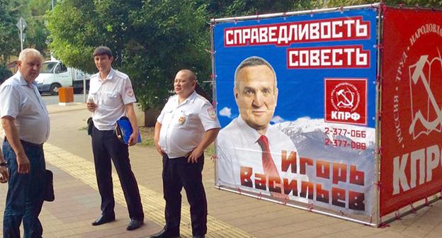 Сотрудники полиции на фоне символики КПРФ и портрета кандитата в ЗСК И. Васильева. Фото Светланы Кравченко для "Кавказского узла"