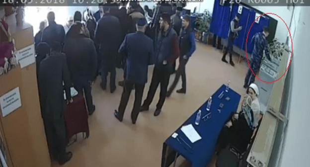 Человек в камуфляже опускает три бюллетеня в урну на избирательном участке в Аргуне. Кадр видео twitter.com/Press_Focusnik/status/975311003201228801