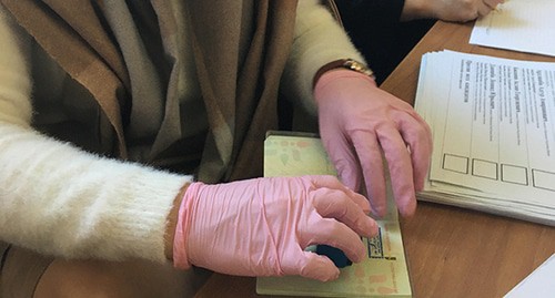 Член избирательной комиссии в медицинских перчатках ставит отметку о голосовании в паспорт. Сухум, 22 марта 2020 года. Фото Анны Грицевич для "Кавказского узла"
