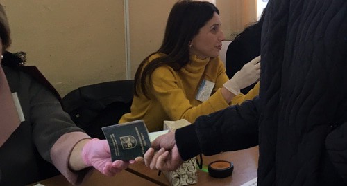 Член избирательной комиссии в медицинских перчатках ставит отметку о голосовании в паспорт. Сухум, 22 марта 2020 г. Фото Анны Грицевич для "Кавказского узла"