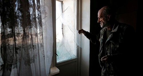 Мужчина убирает остатки стекла из окна, поврежденного обстрелом в Степанакерте 13 октября 2020 года. Фото REUTERS/Stringer