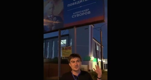  Адлер Туркменов на фоне возмутившего его плаката с изображением Суворова. Стопкадр из видео в в Telegram-канале "Многонационал" https://t.me/mnogonazi/6223.
