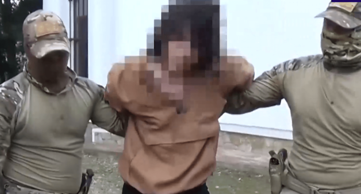 Силовики ведут задержанного в Майкопе. Стоп-кадр видео от 11.07.25, https://t.me/tass_agency/260085
