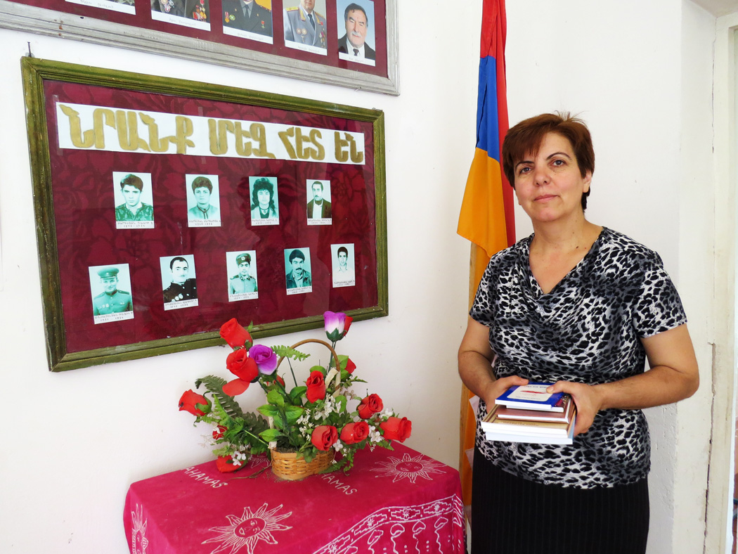 Сусанна Григорян рядом со стендом, где вывешены фотографии погибших сельчан в карабахской войне.