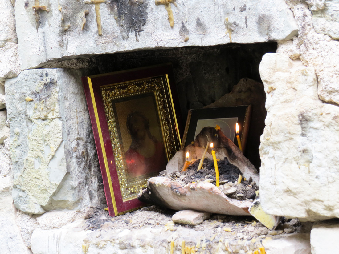 В нише, во внутренней части монастыря, зажигают свечи. Видны иконы.